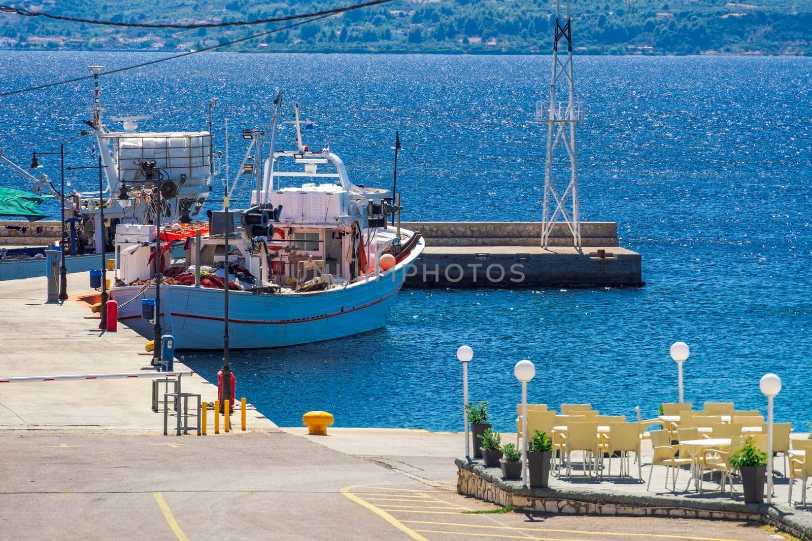 A traditional caique fishing boat with gear moored at a small port around a calm blue sea in Greece.