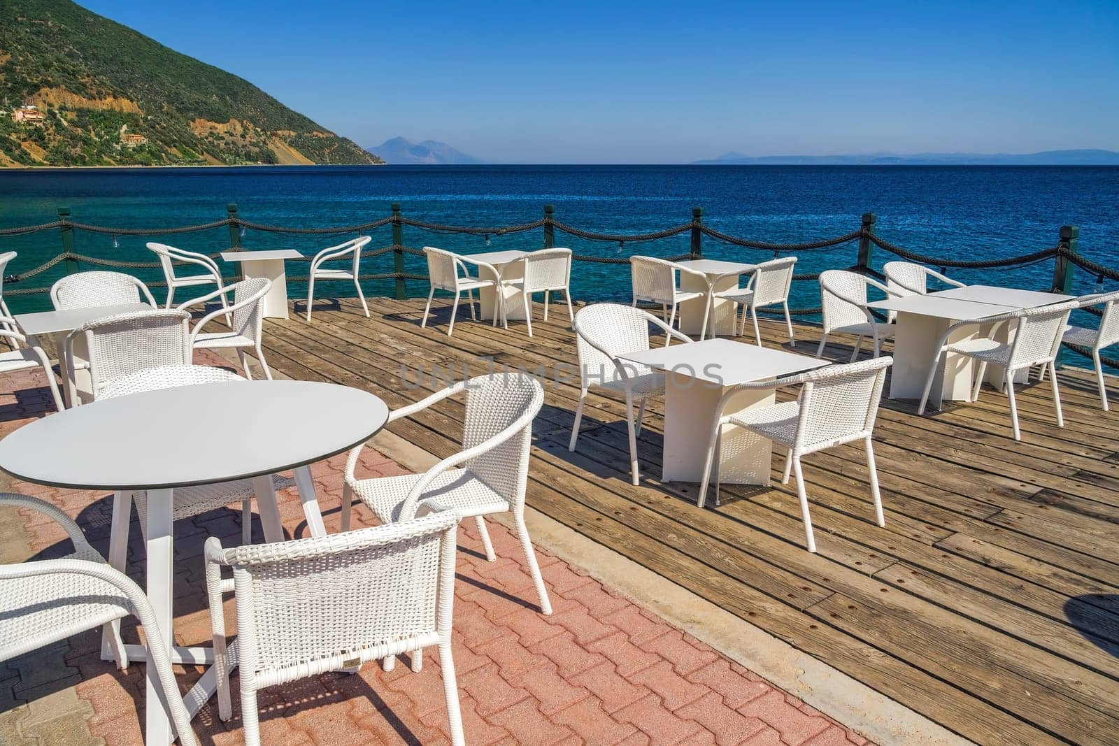 Empty cafe with chairs and tables by the seafront under a blue sky in summer.