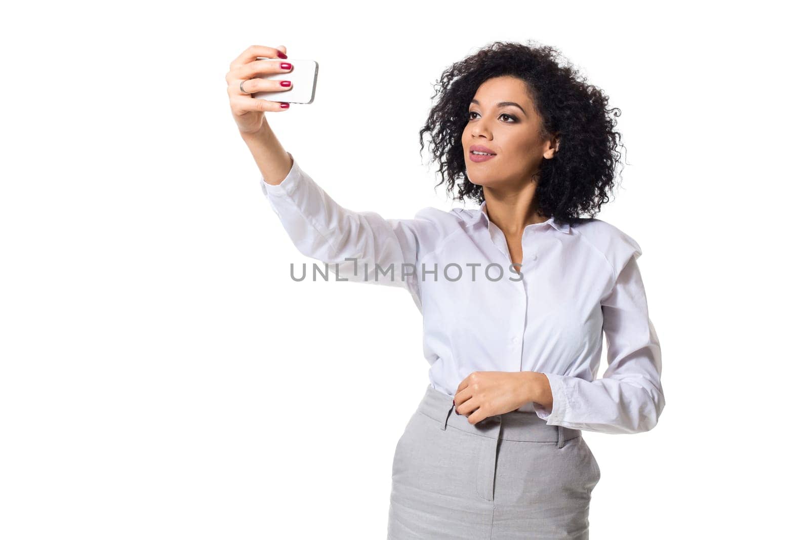 Beautiful brunette woman in classic white shirt and skirt make selfie on the phone. White background. Isolated