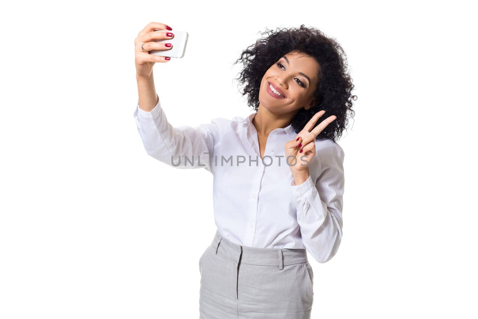 Beautiful brunette woman in classic white shirt and skirt make selfie on the phone. White background. Isolated