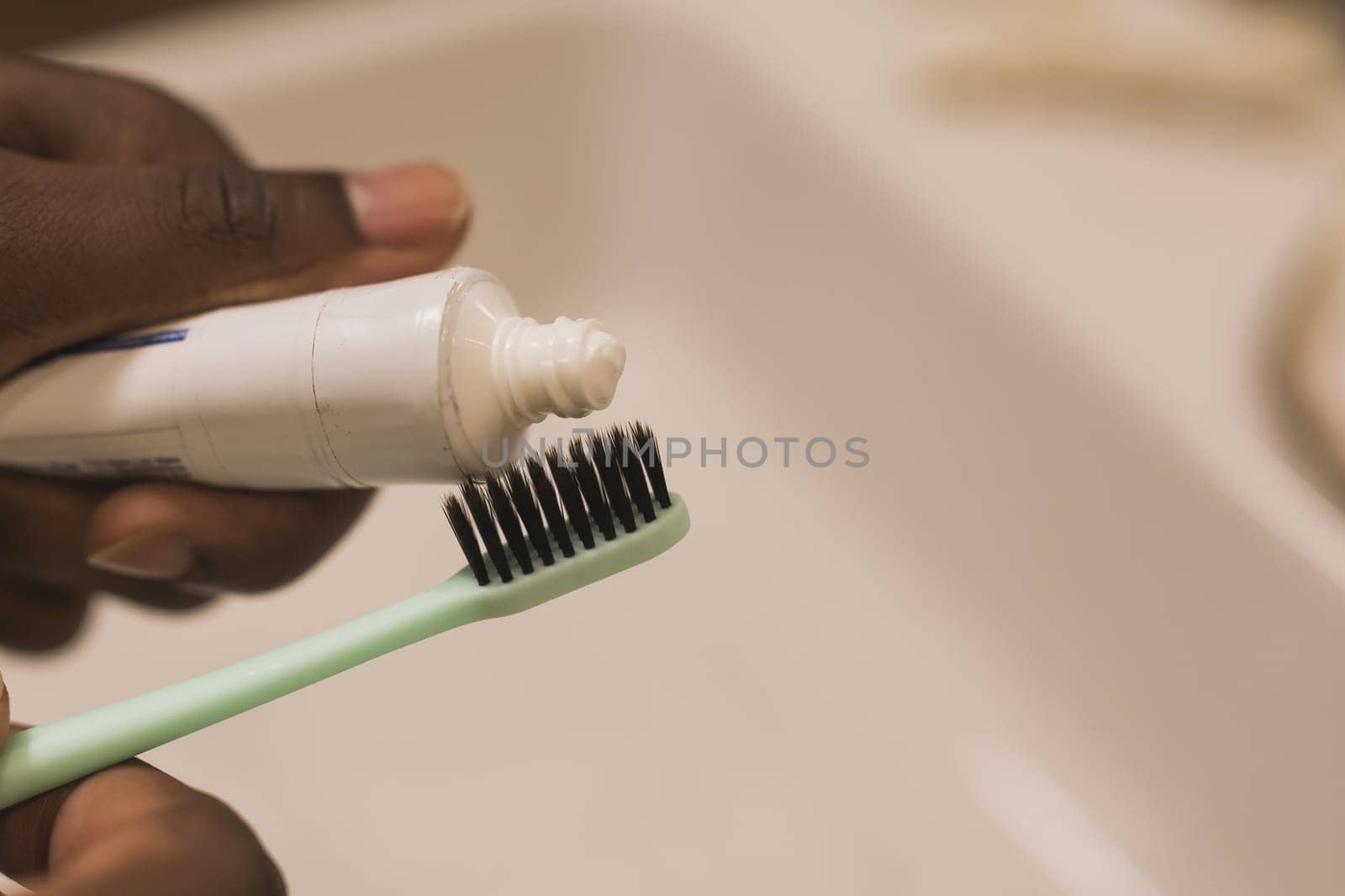 African american male hand holding toothbrush with toothpaste applied on it in bathroom. Close up of man hand ready for brushing teeth. Guy hand holding toothbrush with white tooth paste. by Satura86