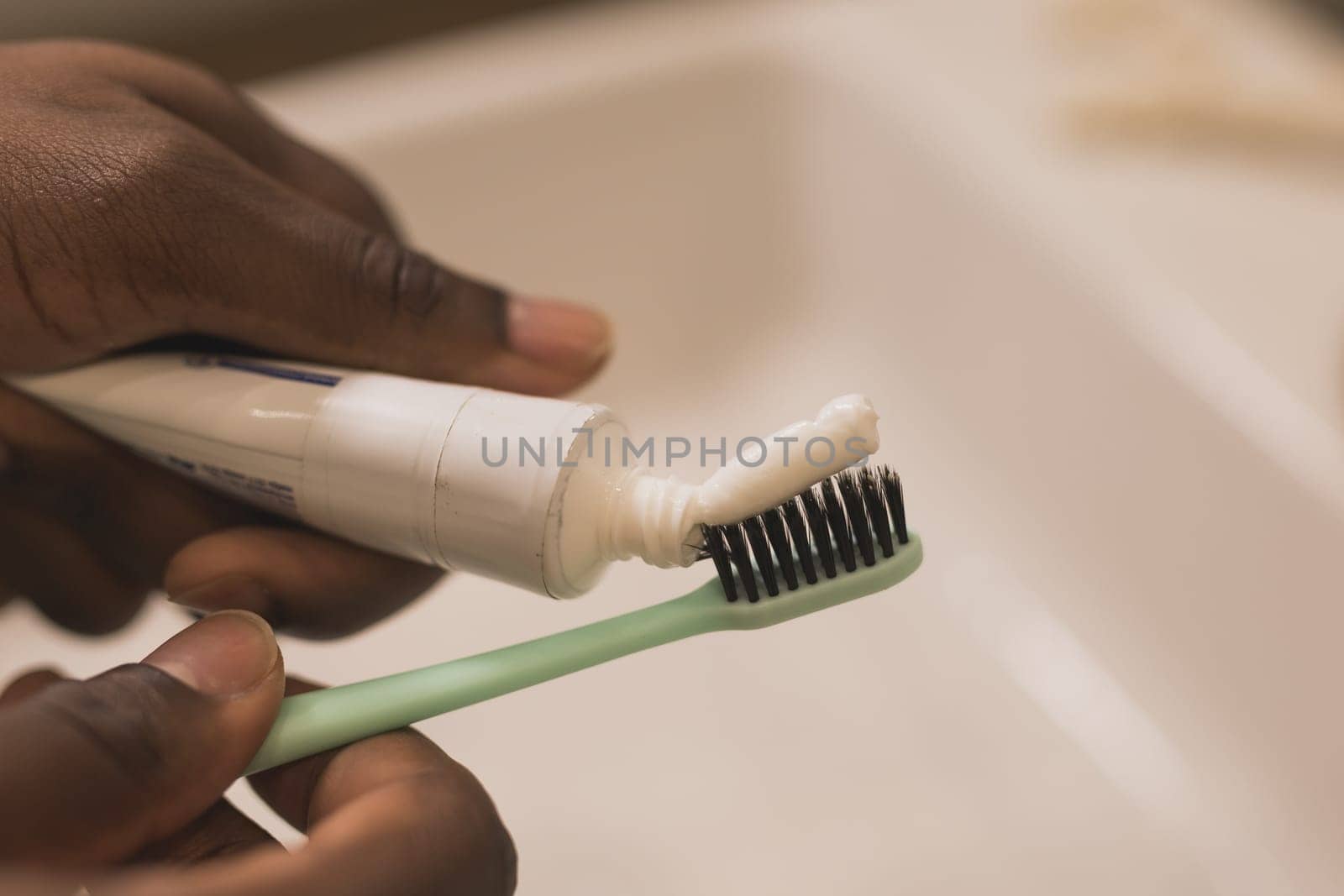 African american male hand holding toothbrush with toothpaste applied on it in bathroom. Close up of man hand ready for brushing teeth. Guy hand holding toothbrush with white tooth paste. by Satura86