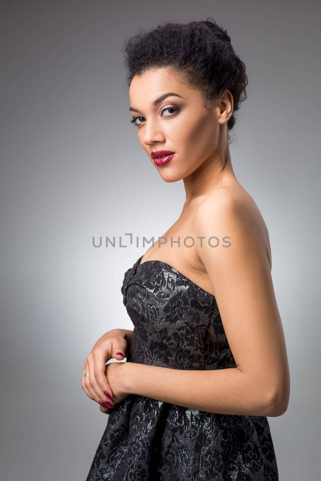 Portrait of beautiful brunette girl in the studio on a gray background in a black dress. She looks into the camera