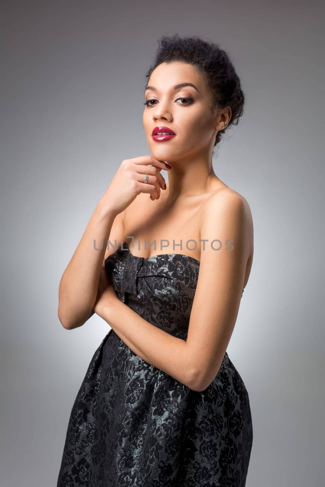 Portrait of beautiful brunette girl in the studio on a gray background in a black dress