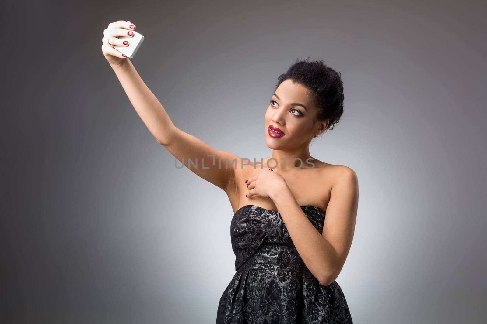 Portrait of a Beautiful brunette doing selfie in a black dress on a light background