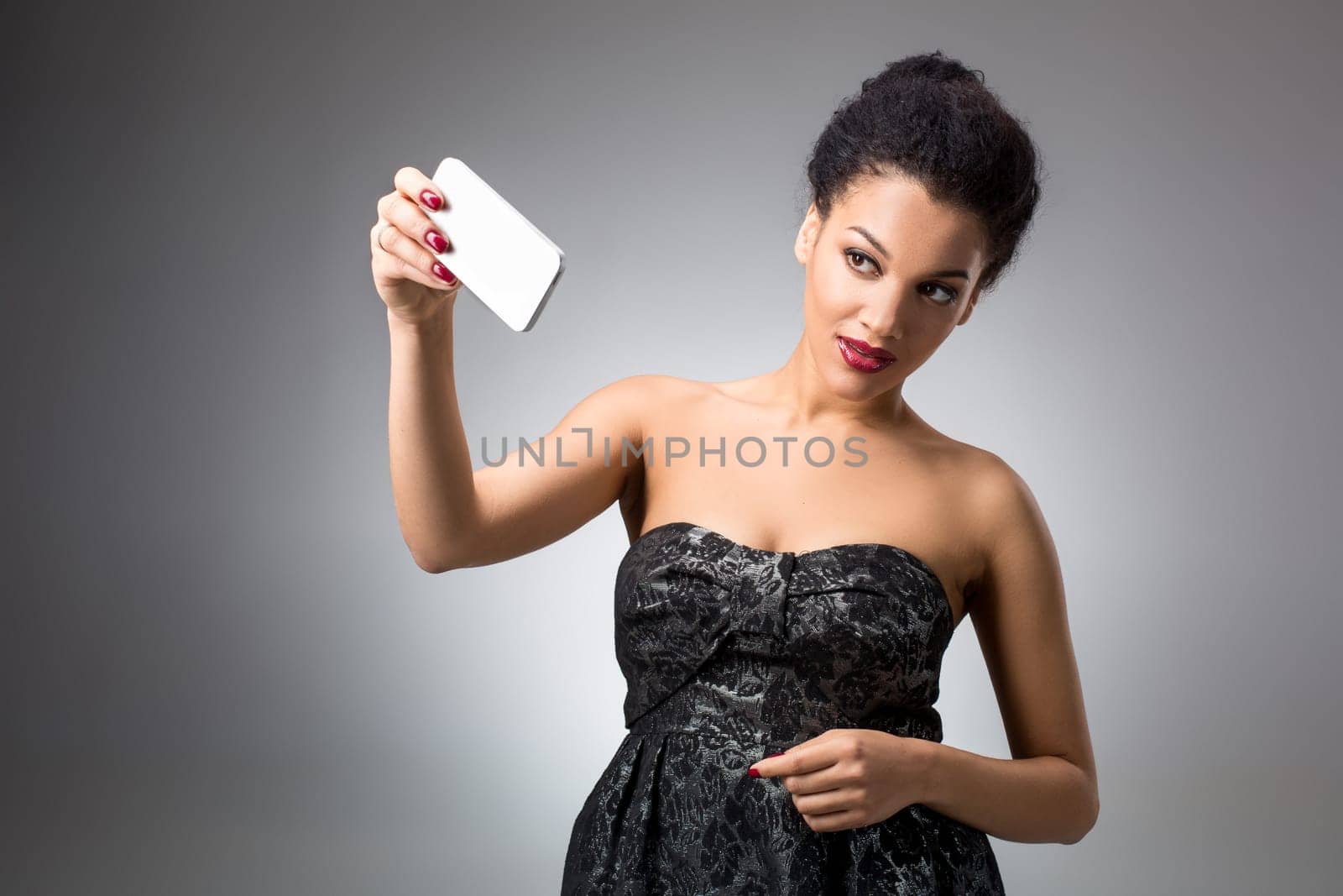 Portrait of a Beautiful brunette doing selfie in a black dress on a light background