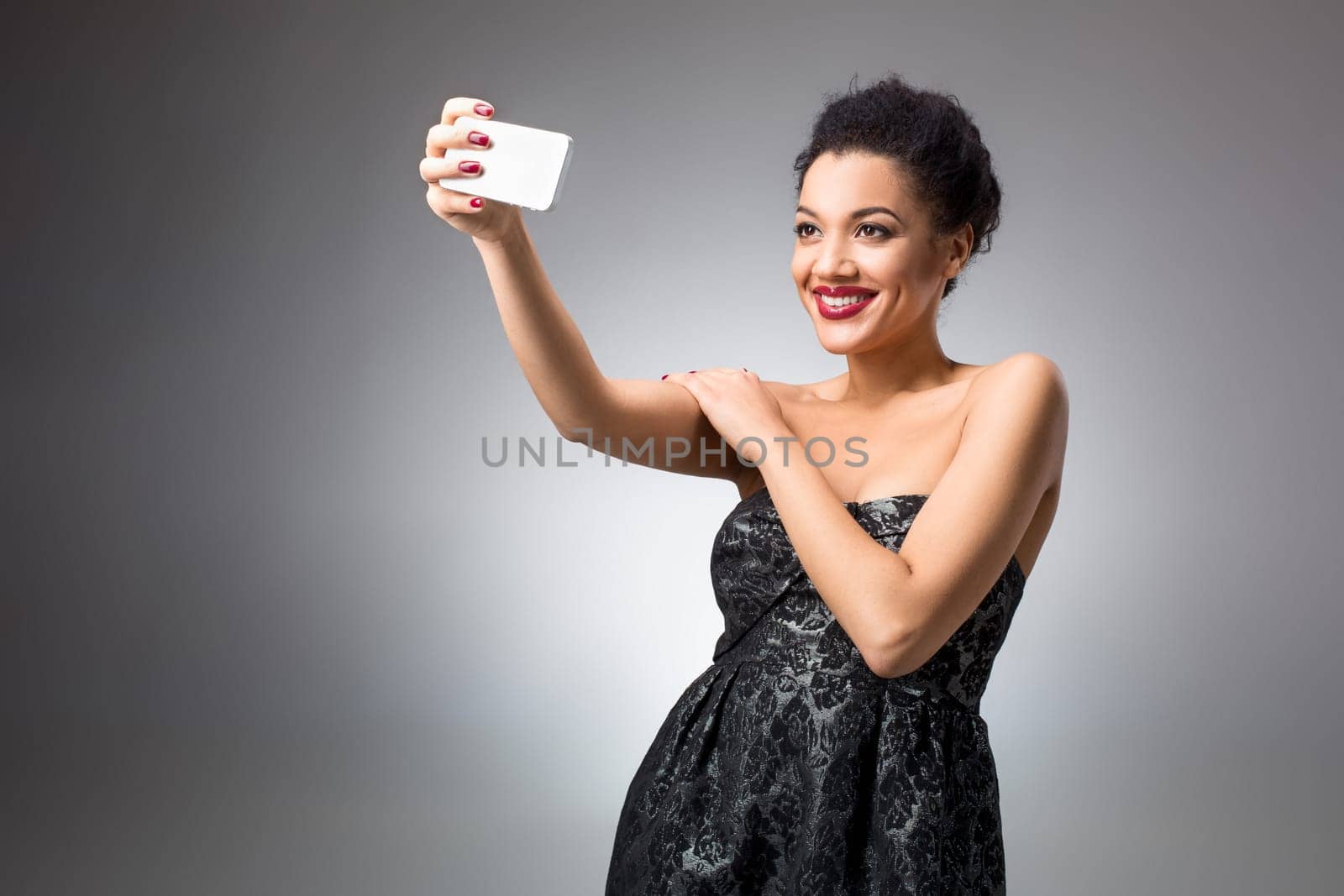 Portrait of a Beautiful brunette doing selfie in a black dress on a light background