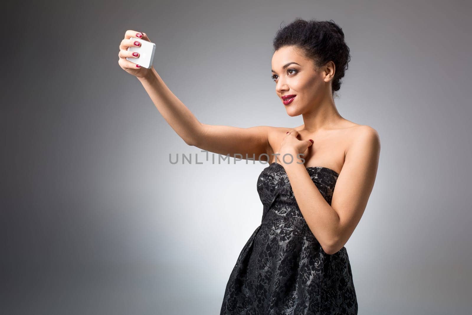 Portrait of a Beautiful brunette doing selfie in a black dress on a light background