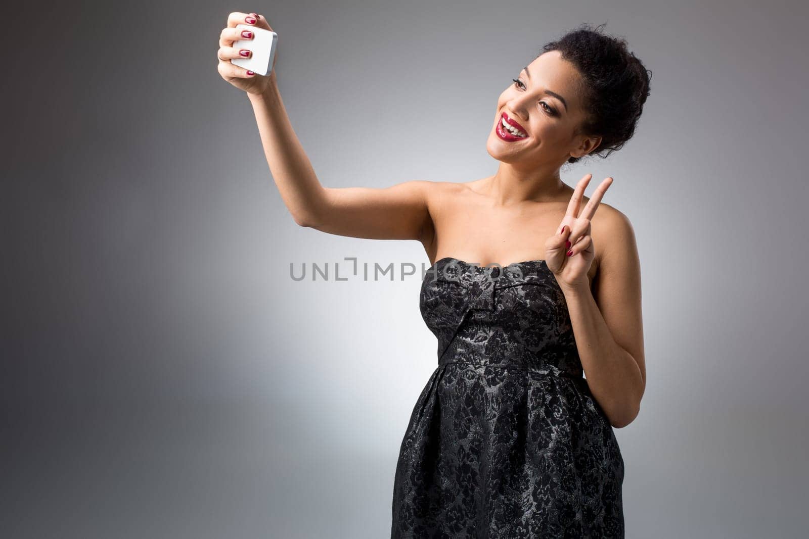 Portrait of a Beautiful brunette doing selfie in a black dress on a light background