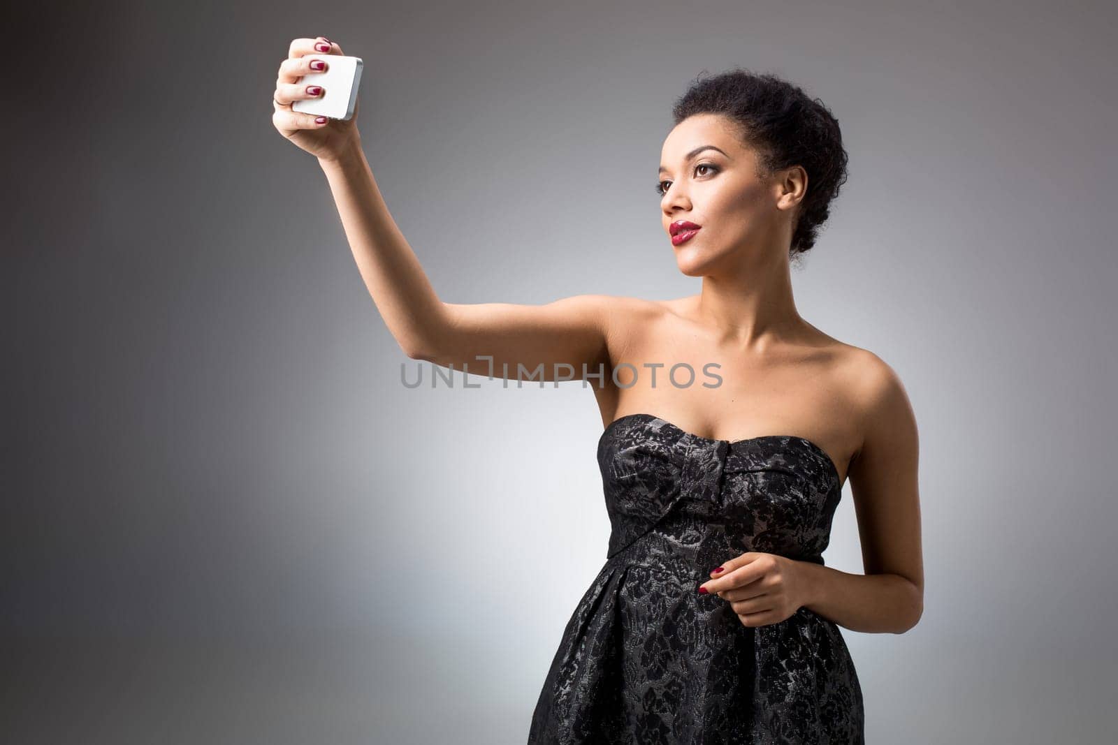 Portrait of a Beautiful brunette doing selfie in a black dress on a light background