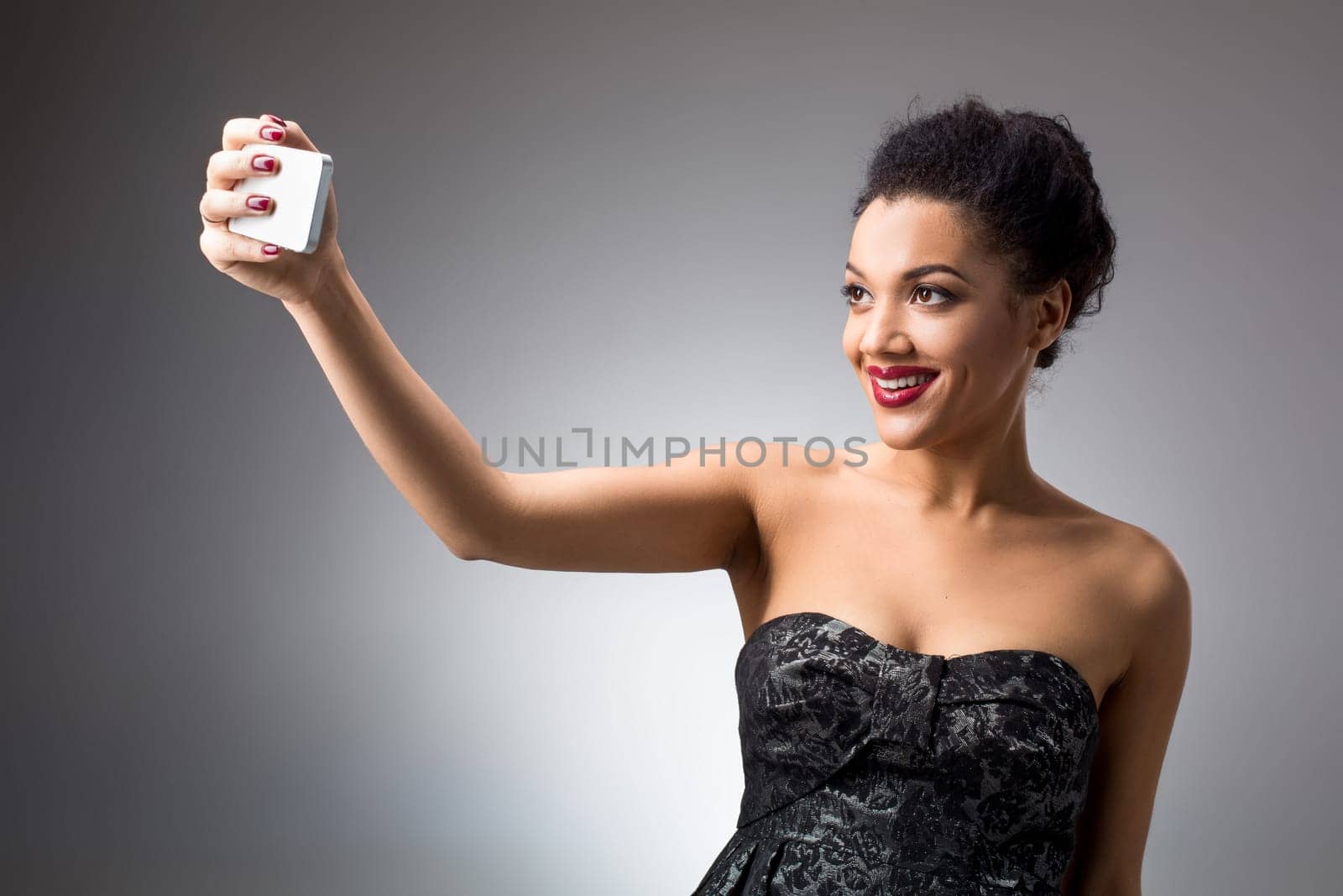 Portrait of a Beautiful brunette doing selfie in a black dress on a light background