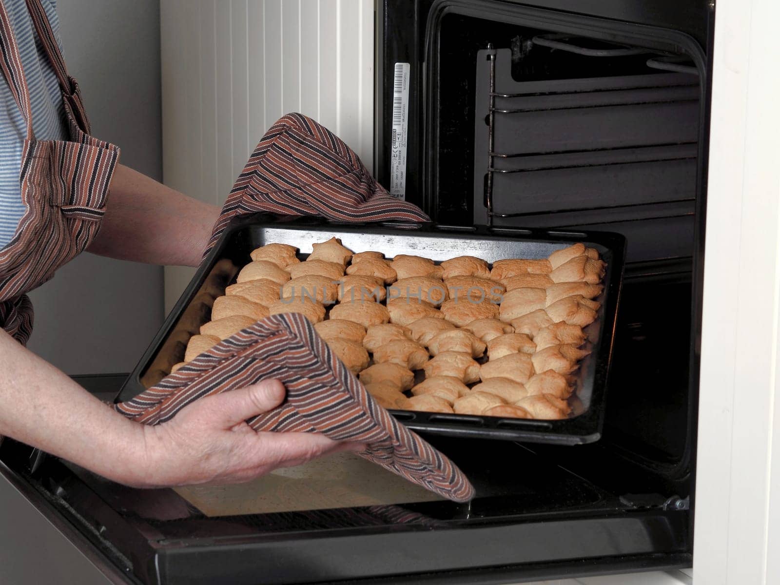 A woman takes a baking sheet with delicious homemade cookies out of the oven. The concept of fresh homemade baking. by TatianaPink