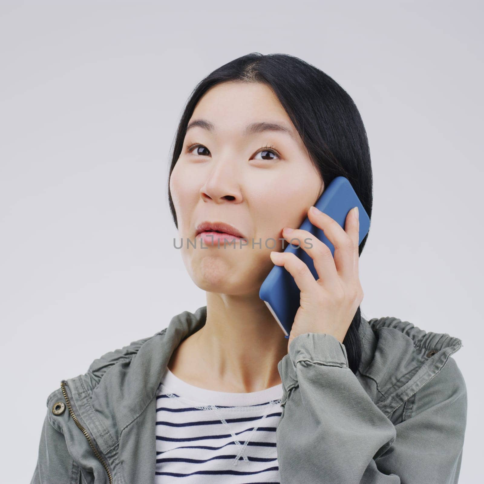 Gossip, phone call and Asian woman talking in studio isolated on a white background. Listening, cellphone and female person speaking, discussion or communication for conversation, news or online chat by YuriArcurs