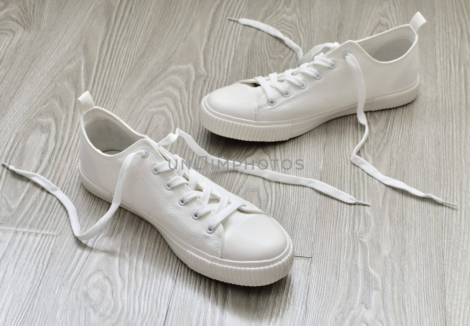 White sneakers with untied laces are on the floor