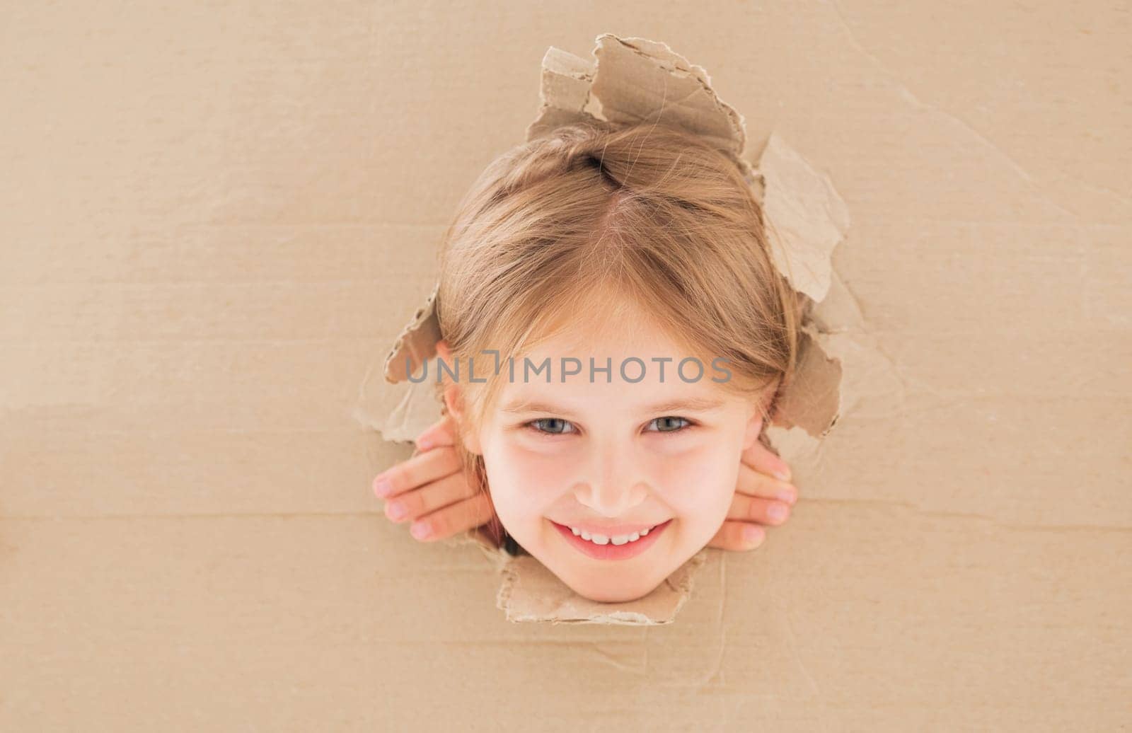 Smiling little girl peeping from hole in cardboard box