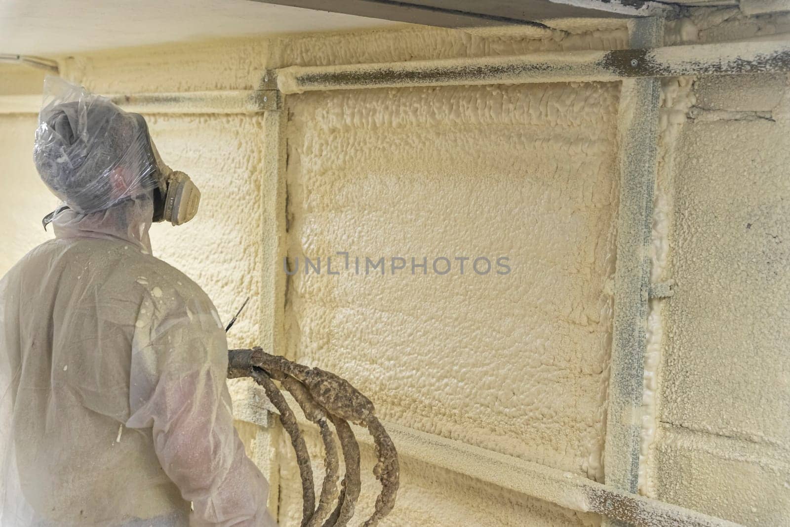 A worker in a protective suit insulates the walls of the basement of the house with polyurethane foam spraying it from a nozzle. filling the walls with foam insulation. Energy saving, warm modern house. modern technologies
