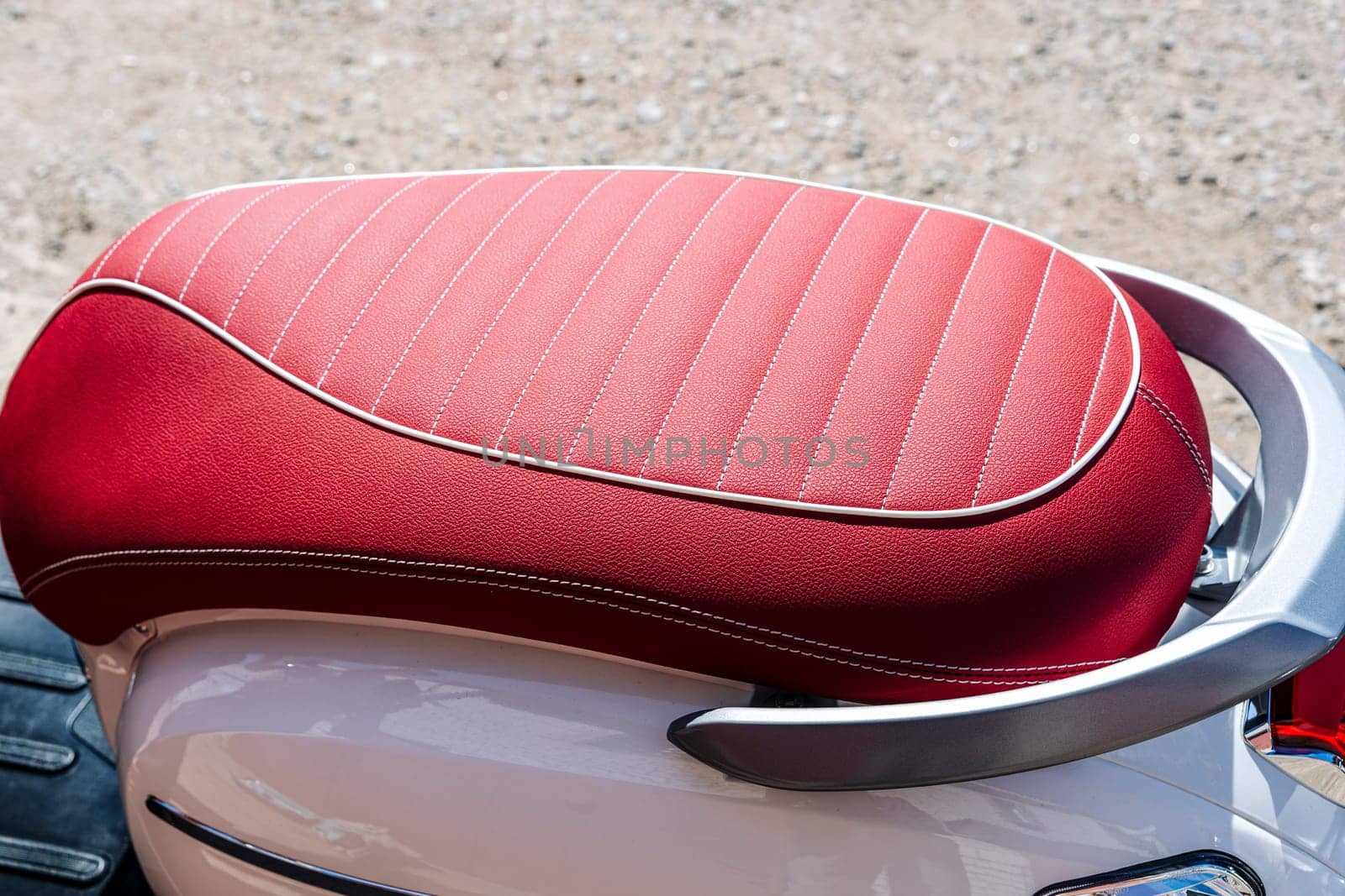 gorgeous red leather motorcycle seat with white stitching. the scooter seat is made of red leather. Part of a motorcycle. background with red leather texture. Texture, artificial leather with stitching