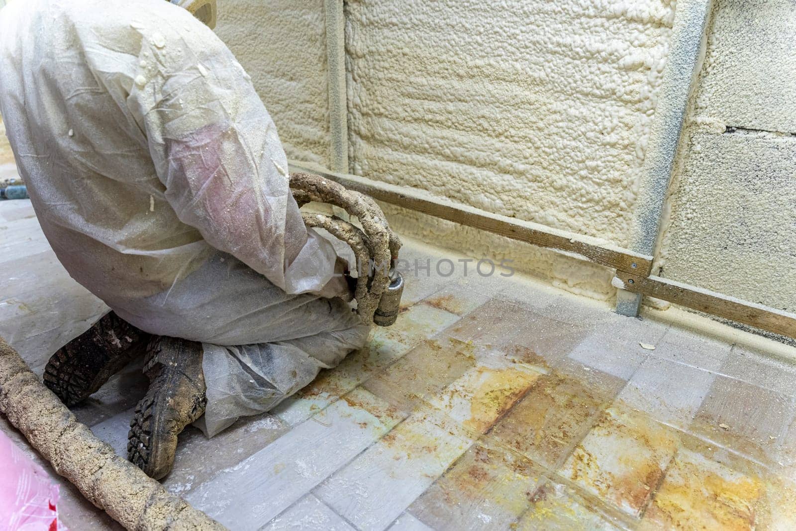 A worker in a protective suit insulates the walls of the basement of the house with polyurethane foam spraying it from a nozzle. filling the walls with foam insulation. Energy saving, warm modern house. modern technologies