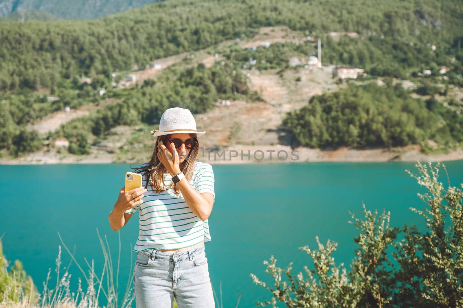Woman taking selfie on mobile phone of mountains lake background. Traveler female having video chat on cellphone on the blue lake outdoors travel adventure vacation by Ostanina