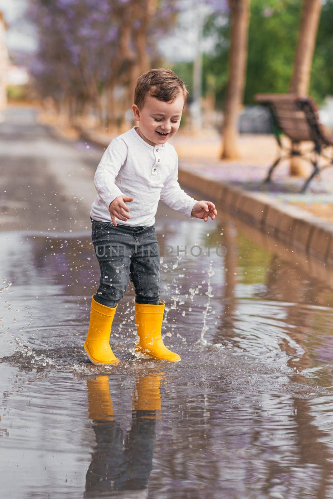 boy in yellow rubber boots jumping over a puddle in the rain.