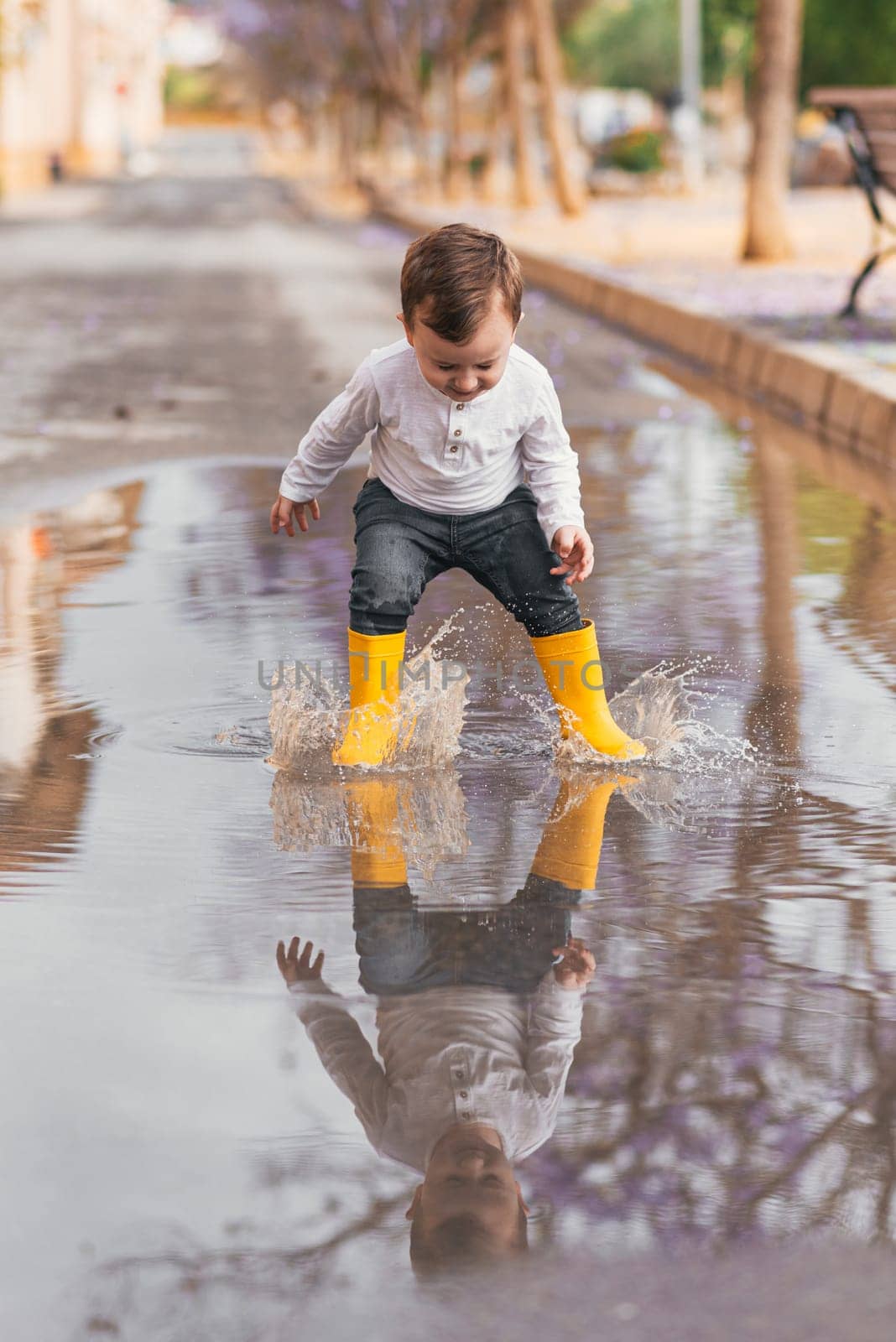 boy in yellow rubber boots jumping over a puddle in the rain by jcdiazhidalgo