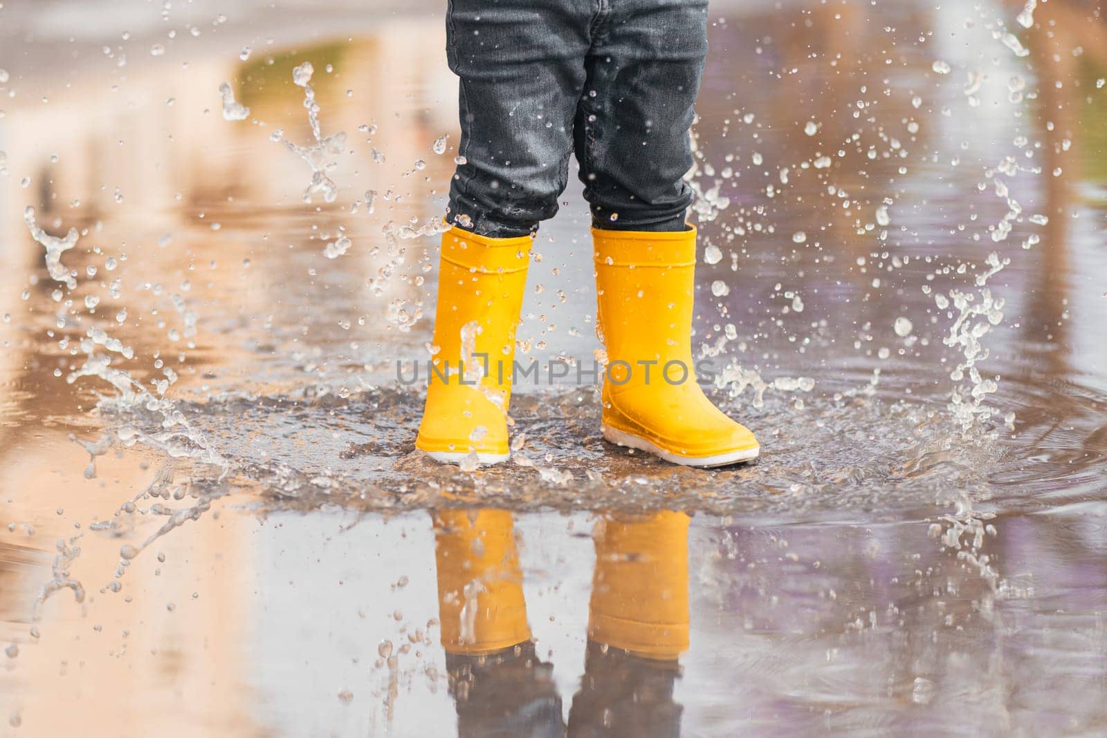 Child's feet in yellow rubber boots jumping over a puddle in the rain by jcdiazhidalgo