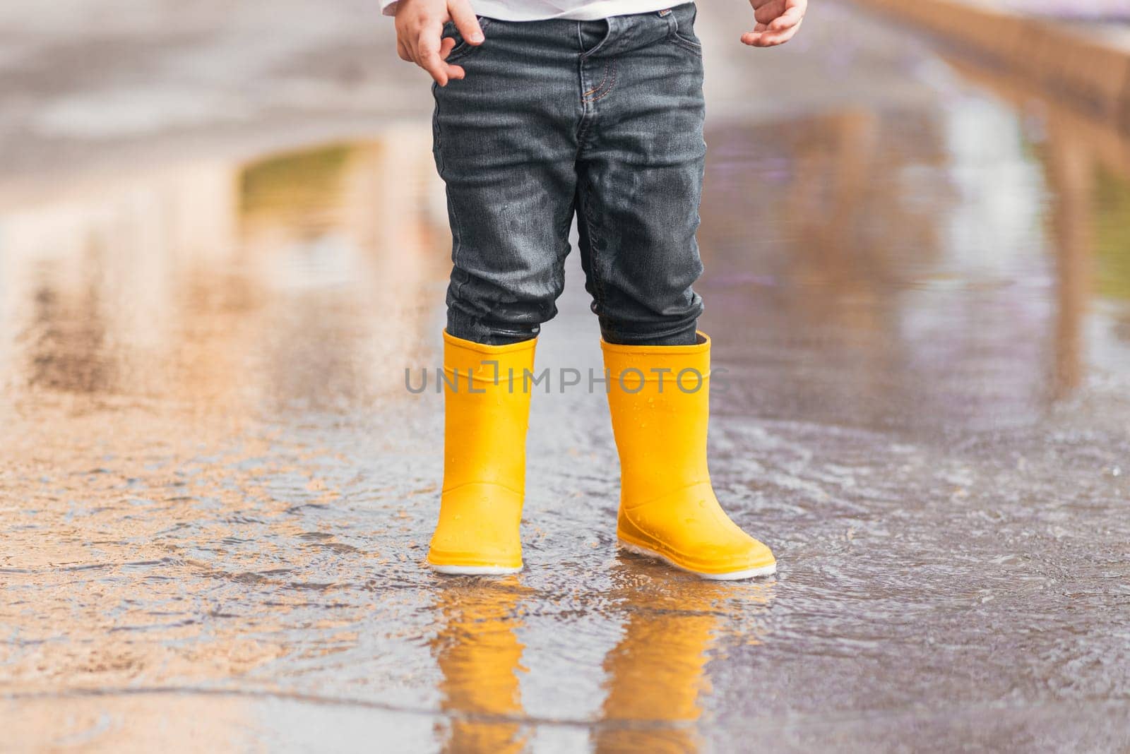 Child's feet in yellow rubber boots jumping over a puddle in the rain by jcdiazhidalgo