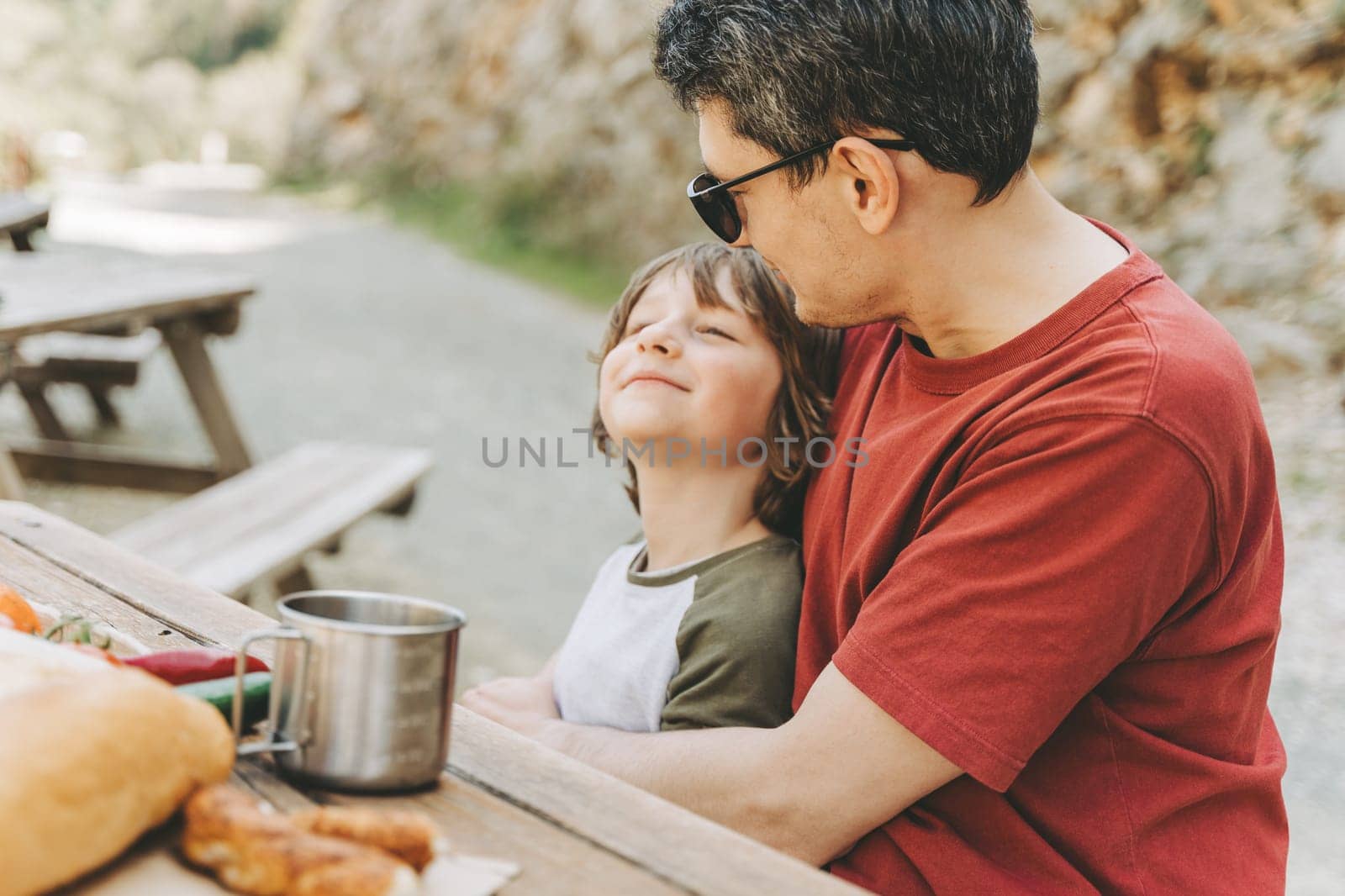 Close-up view of father hugs his school boy son on a family picnic in the mountains. Child kid and his dad taking a rest and enjoying a picnic while hiking in the mountains.
