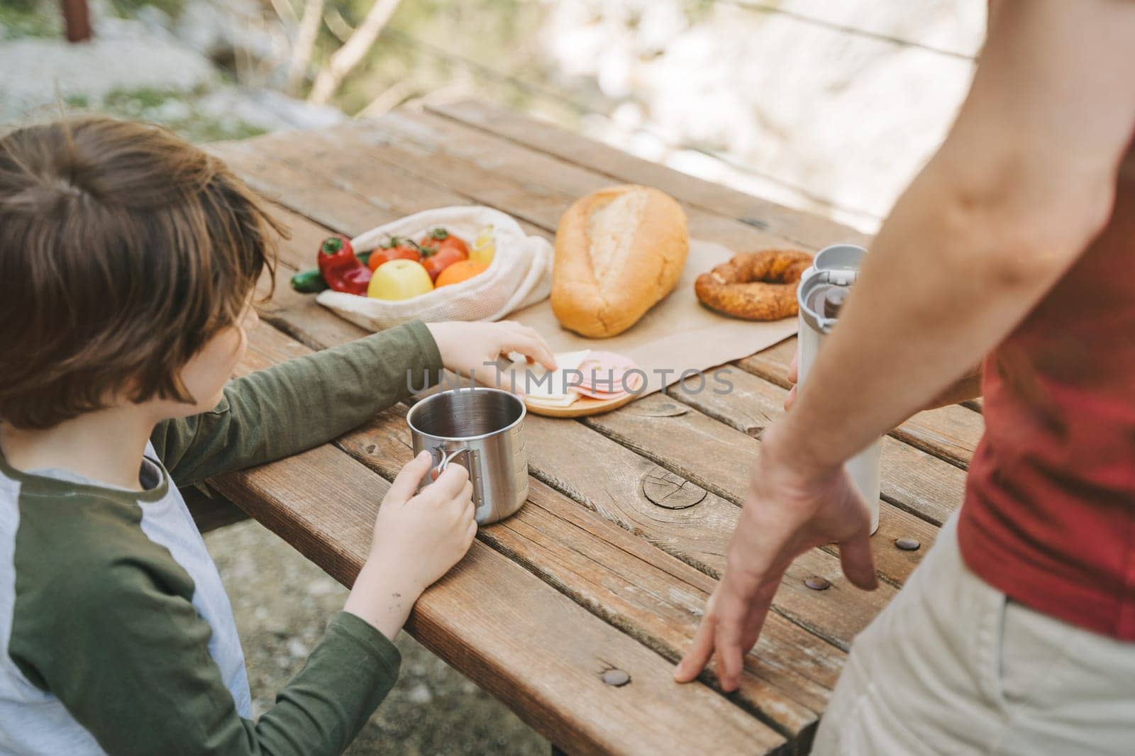 Close-up view of father and his school boy son on a family picnic in the mountains. Child kid and his dad taking a rest and enjoying a picnic while hiking in the mountains.