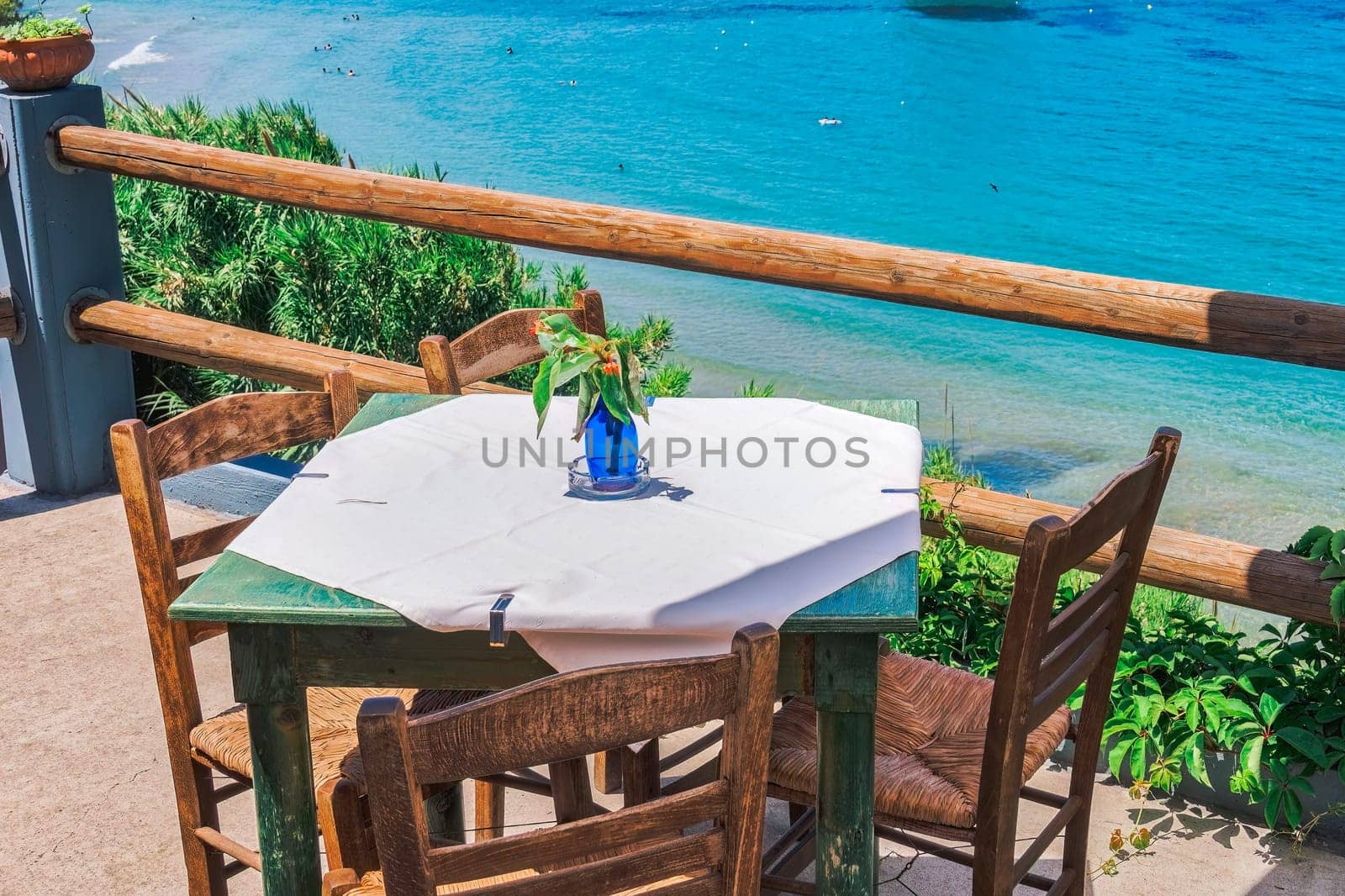 Empty tavern restaurant with wooden chairs and a table by a calm seafront on a bright summer day.