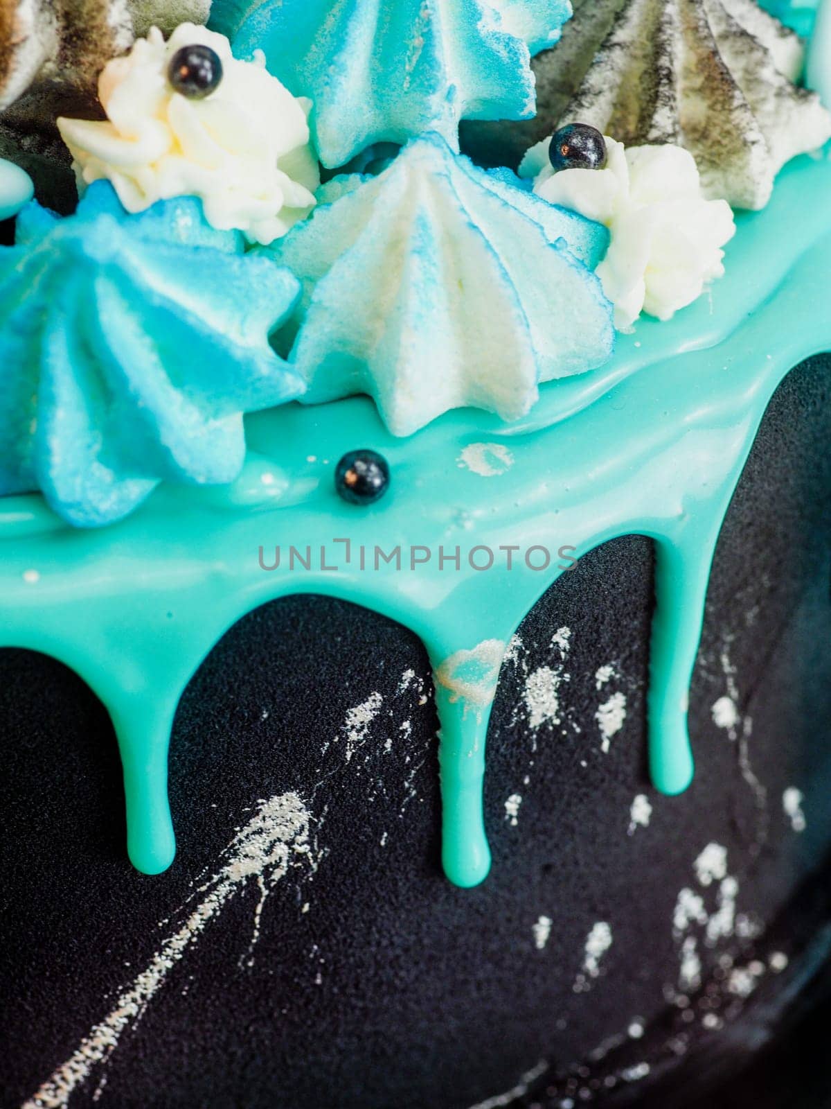 frosted black painted cup cake with blue turquoise dripping and colored handmade meringue topping studio white isolated background