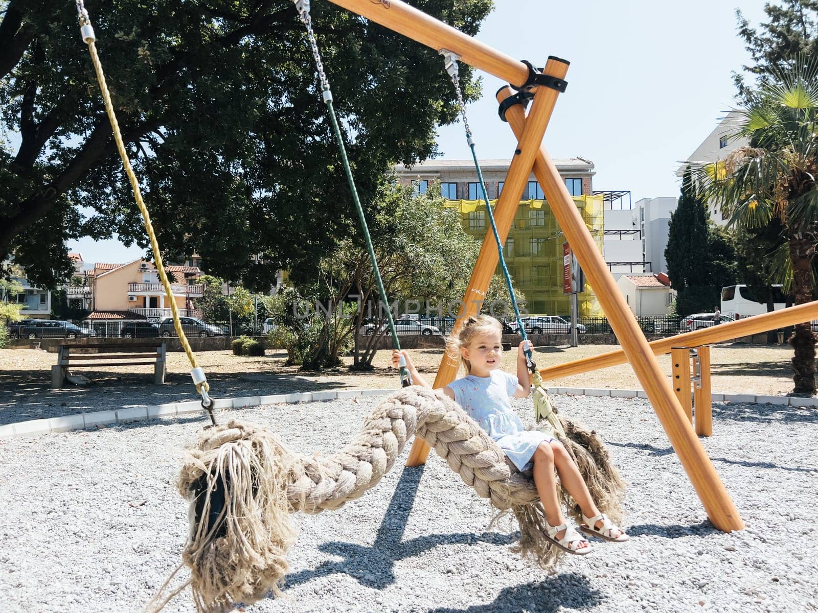 Little girl swings on a swing in the form of a braid on the playground. High quality photo