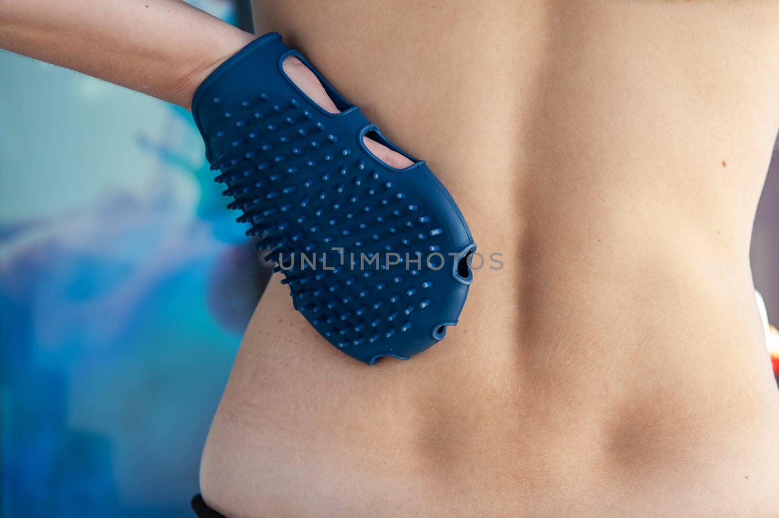 Anticellulite silicone or rubber massager - mitten for body in female hand on body background.