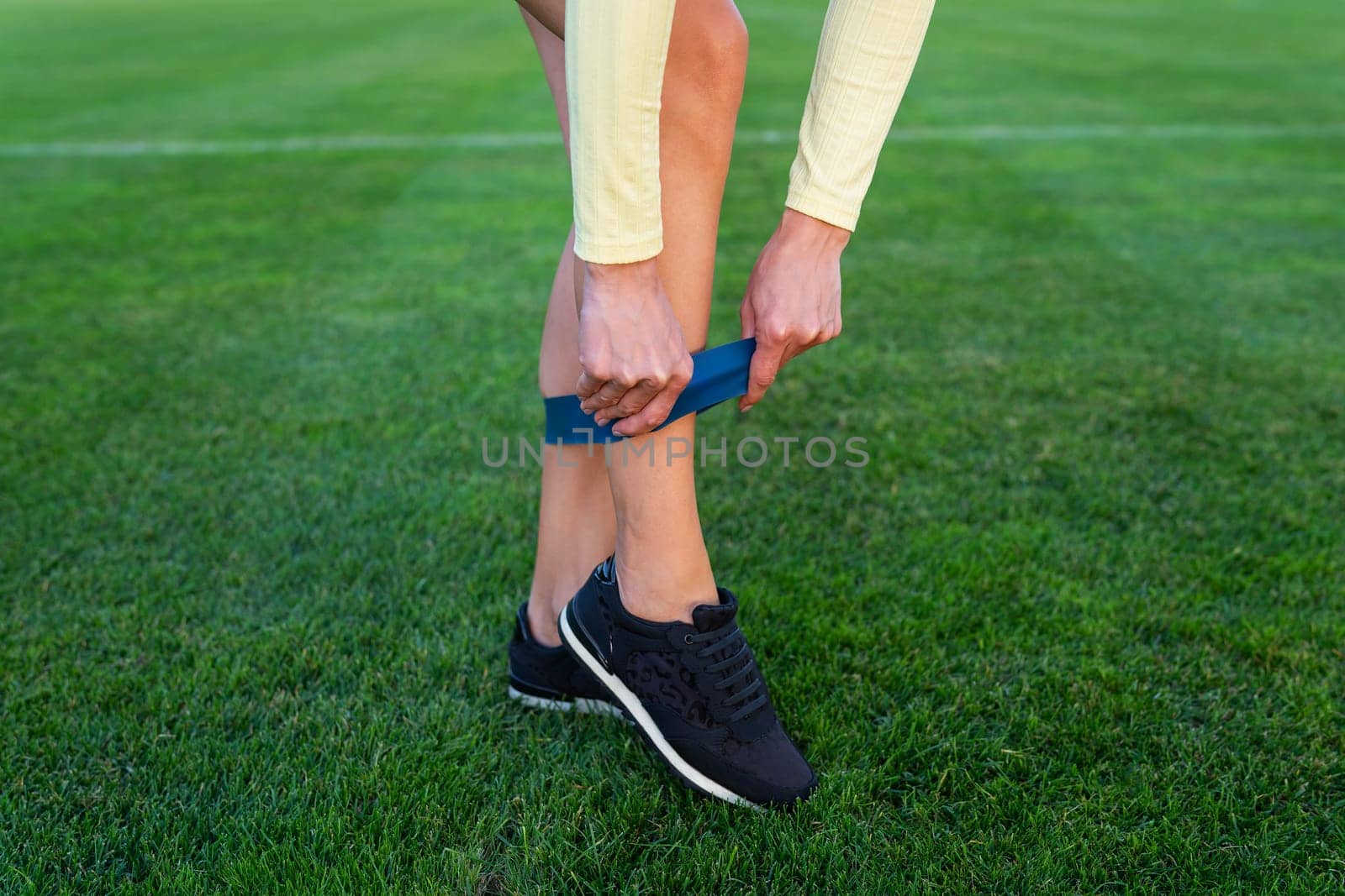 A girl in sneakers starts putting on a sports elastic band at the stadium for sports exercises. Sports and health concept