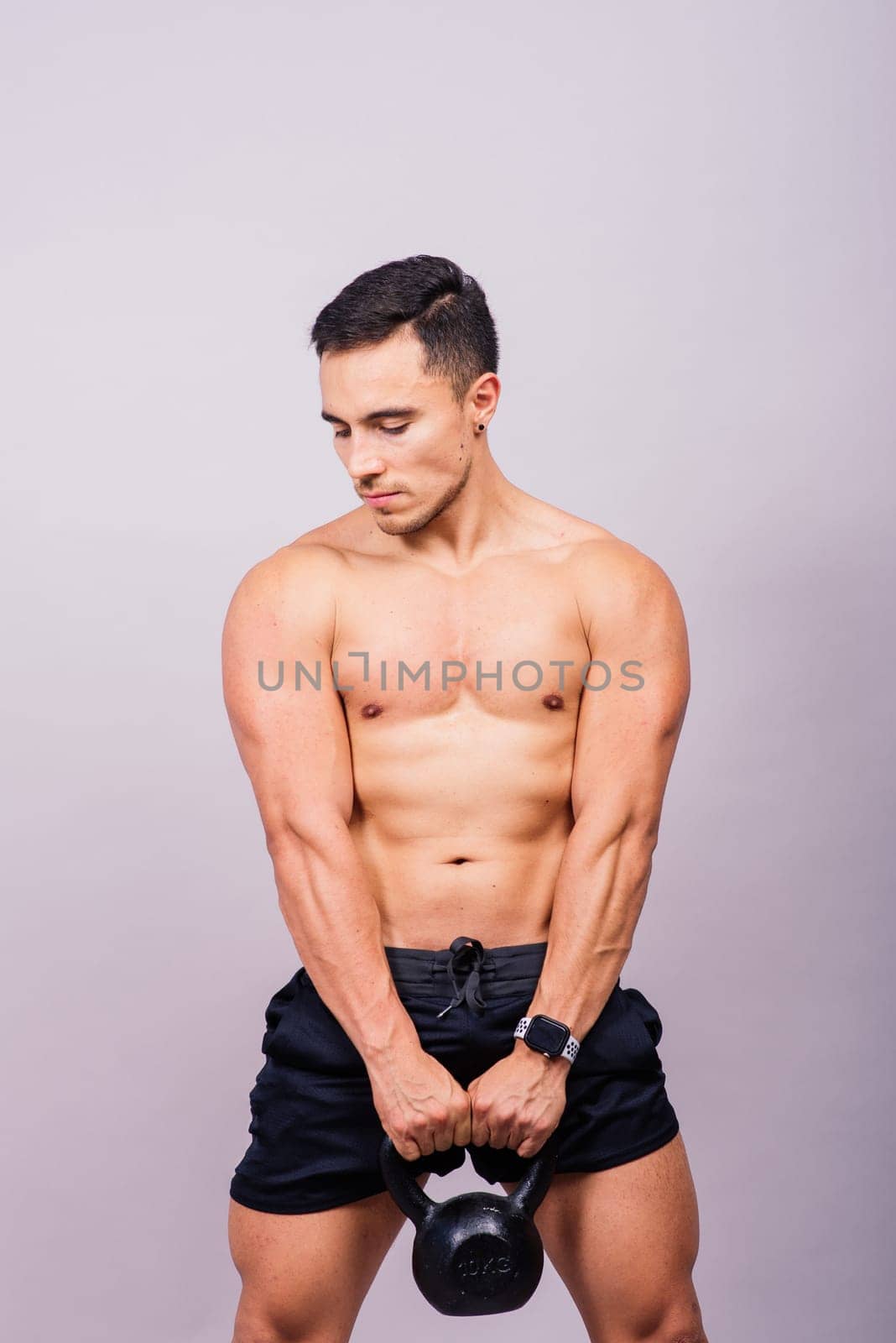 Hispanic male athlete working out with kettlebell on a grey background. Crossfit workout theme.