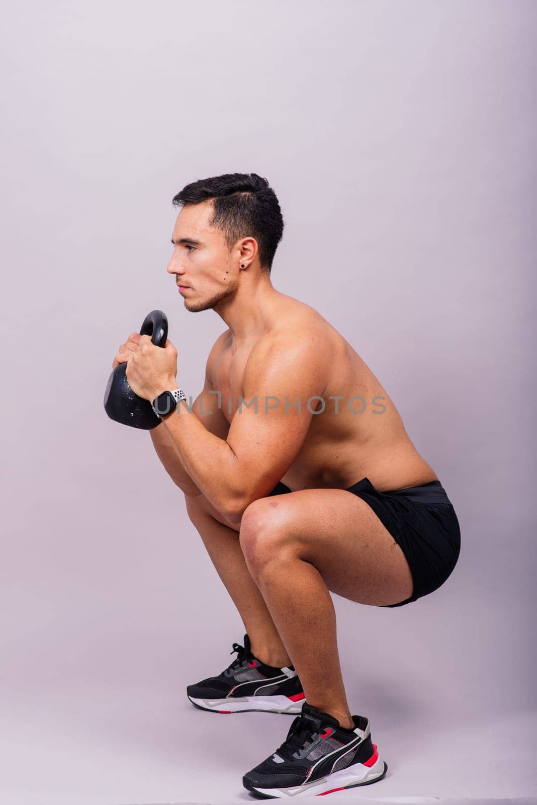 Hispanic male athlete working out with kettlebell on grey background. Crossfit workout theme. by Zelenin