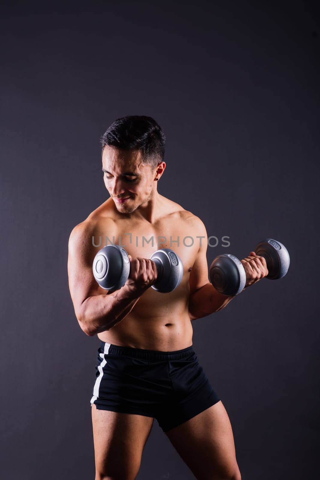 Shirtless bodybuilder showing his great body and holding dumbells.