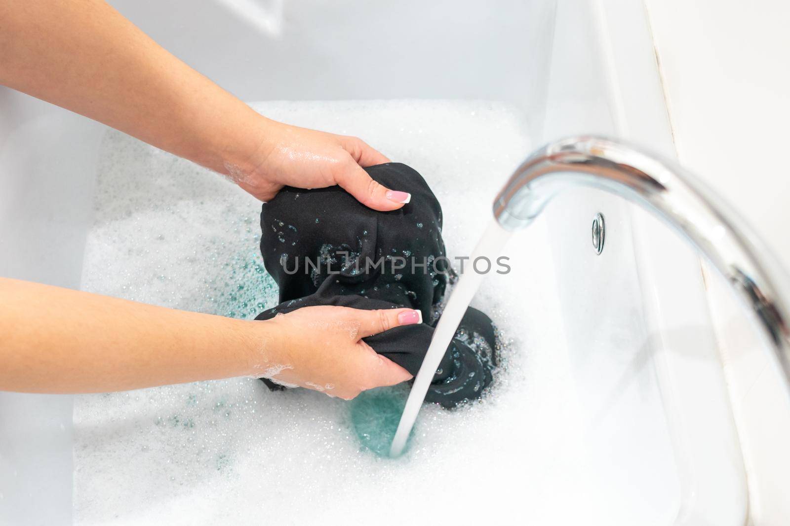 Female hands washing black clothes in basin by Mariakray