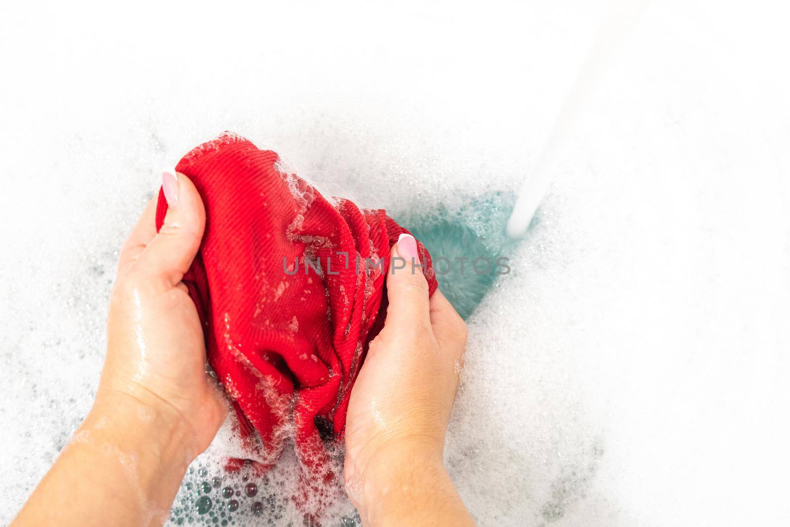 Woman washing red color clothes with detergent foam by Mariakray