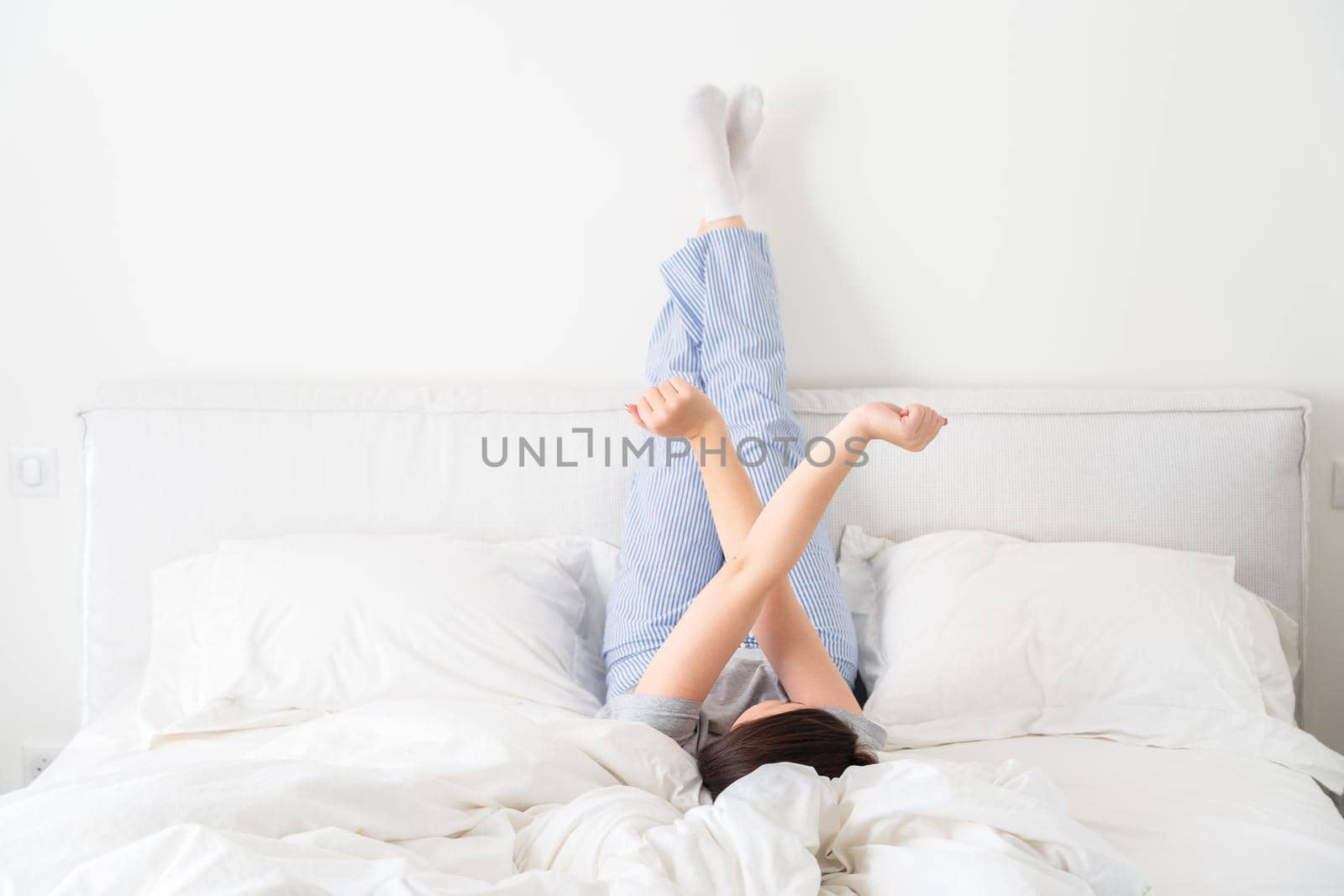 beautiful woman legs raised up high and arms under her head lying on bed in bedroom