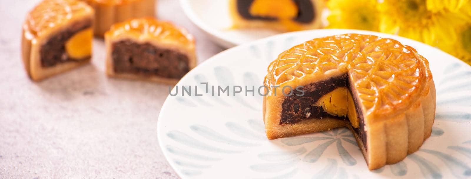 Mid-Autumn Festival traditional food concept - Beautiful cut moon cake on blue pattern plate on white background with flower, close up, copy space