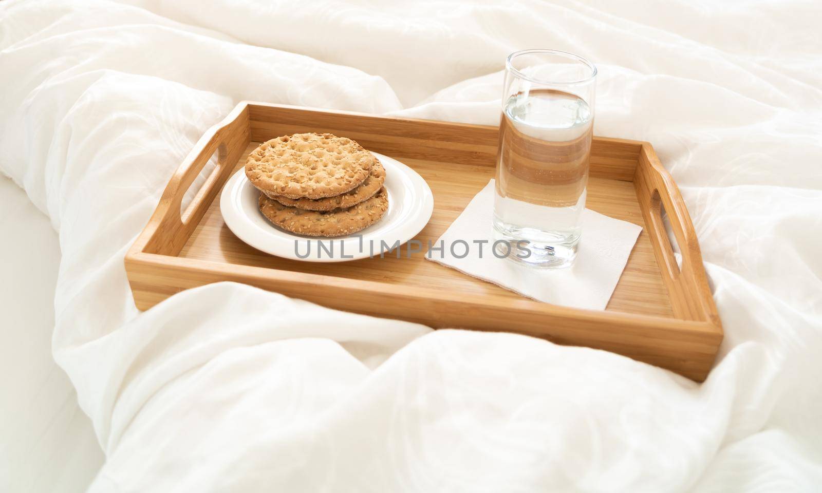 Tray with water and crackers breakfast on a bed by Mariakray