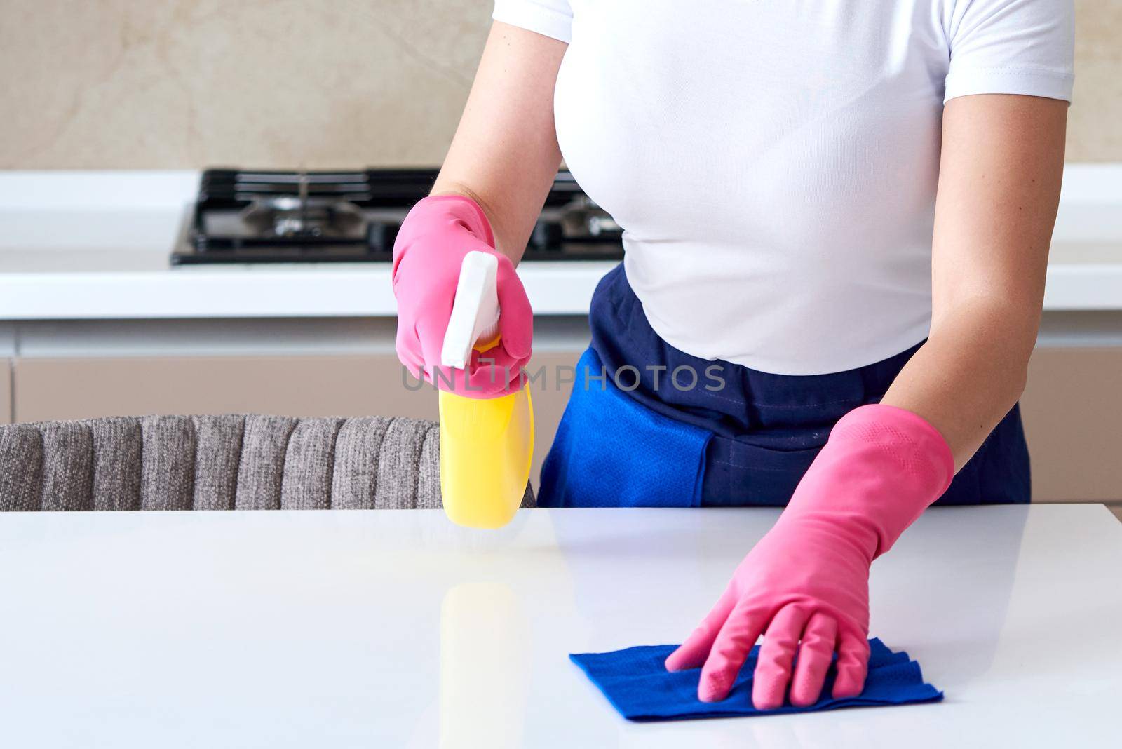 Woman wearing rubber gloves cleaning table with cloth. Disinfecting a kitchen table with bleach
