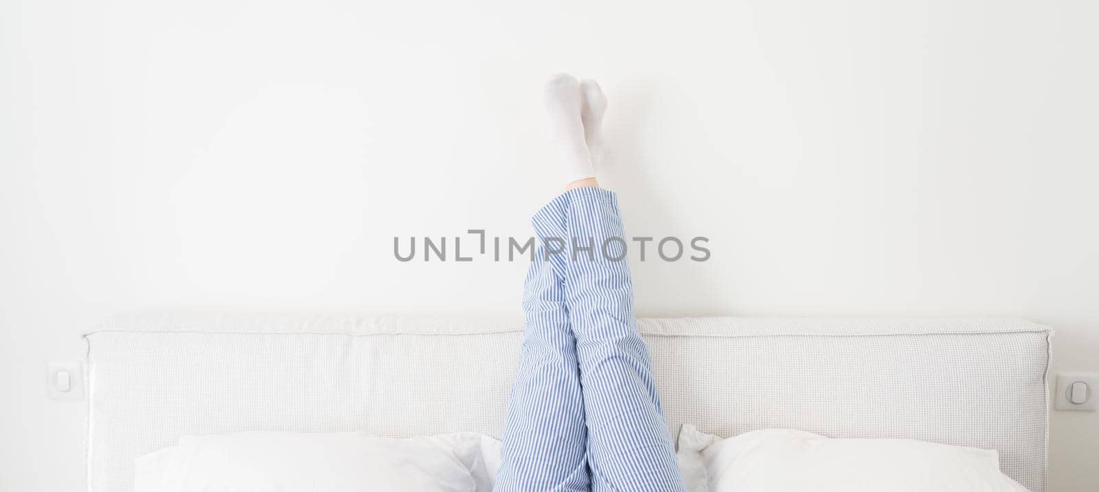 Panorama of female legs raised up high lying on bed in bedroom by Mariakray