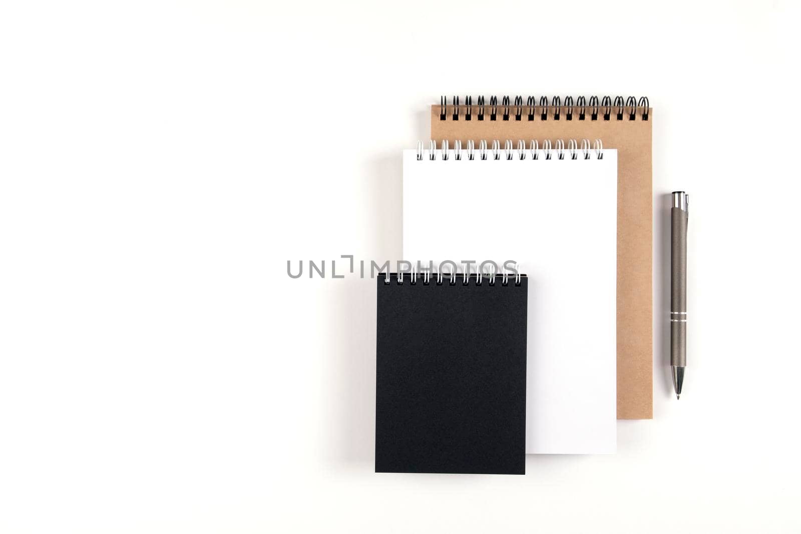 Three blank notepads on a spiral stacked in a stack on a white background. Notebooks with white, black and recycled sheets and pen. Education, office.