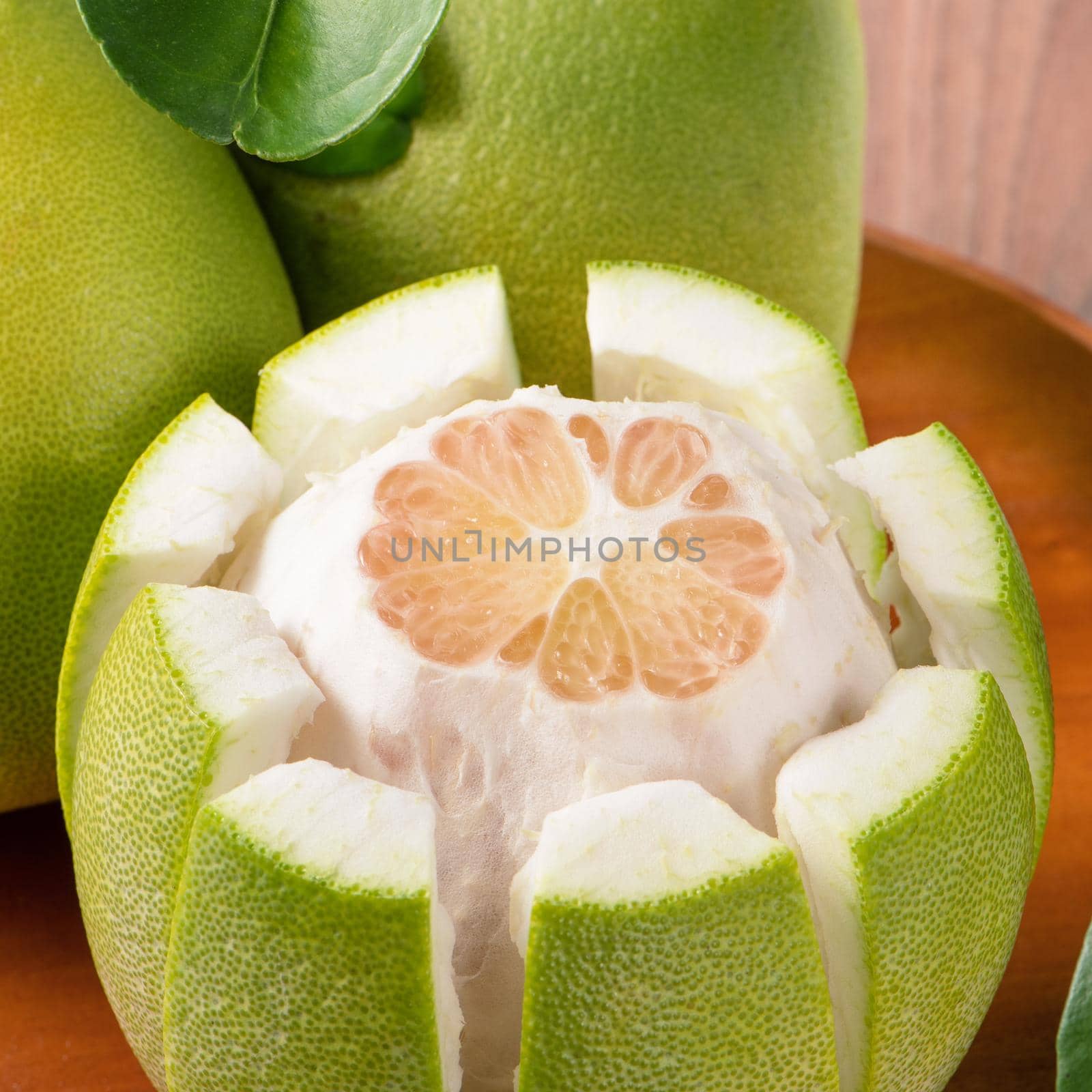 Fresh peeled pomelo, grapefruit, shaddock with green leaves on dark wooden plank table. Seasonal fruit near mid-autumn festival, close up, copy space