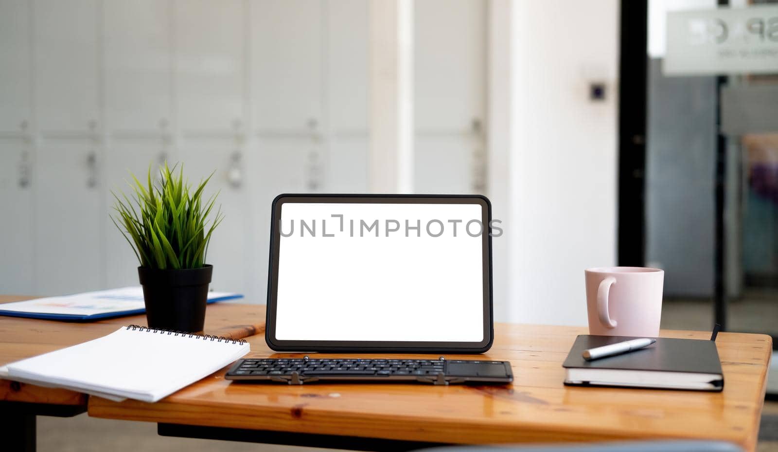 Shot of digital tablet with blank white screen, keyboard, cup of coffee on workspace desk.