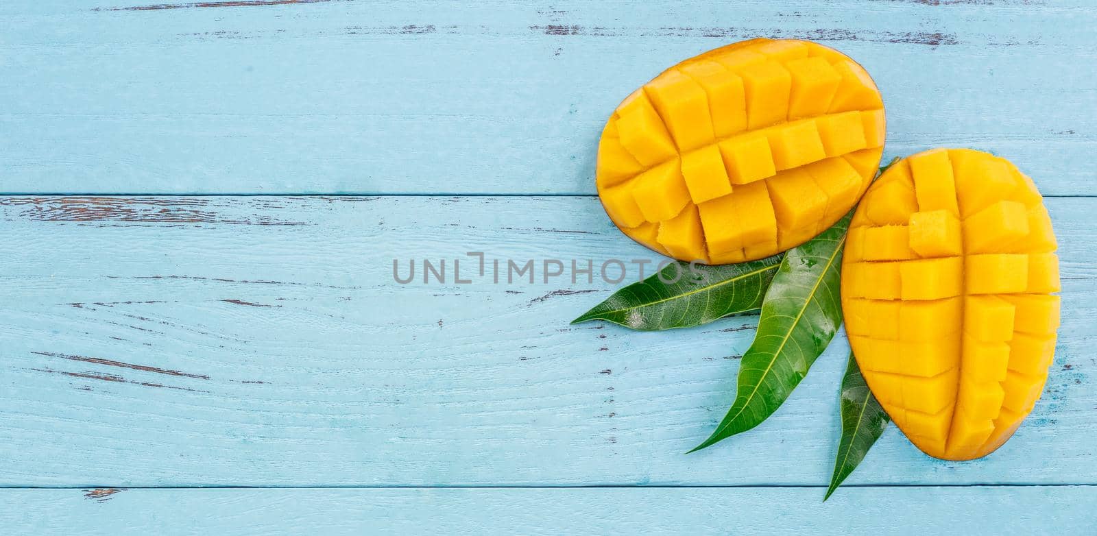 Fresh mango - beautiful chopped fruit with green leaves on bright blue timber background. Tropical fruit design concept. Flat lay. Top view. Copy space