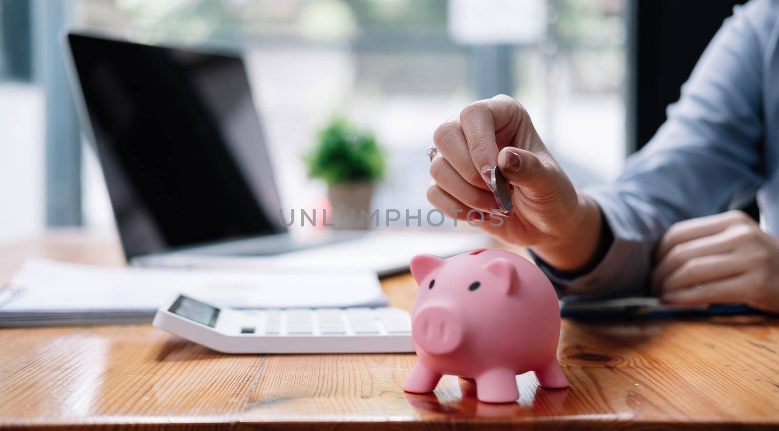 Close up hand of woman putting money coin into pink piggy bank for saving money wealth and financial concept.