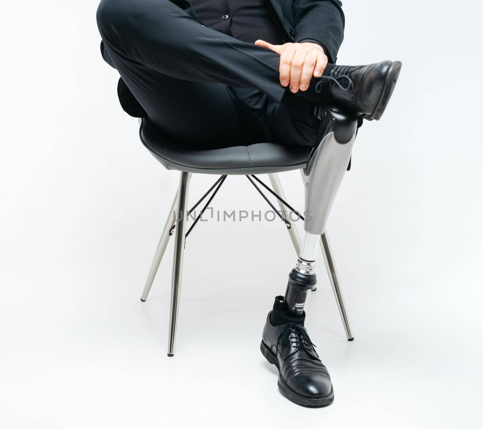 Cropped view of disabled young man with prosthetic leg sitting on a chair in studio, artificial limb concept over white background by Mariakray